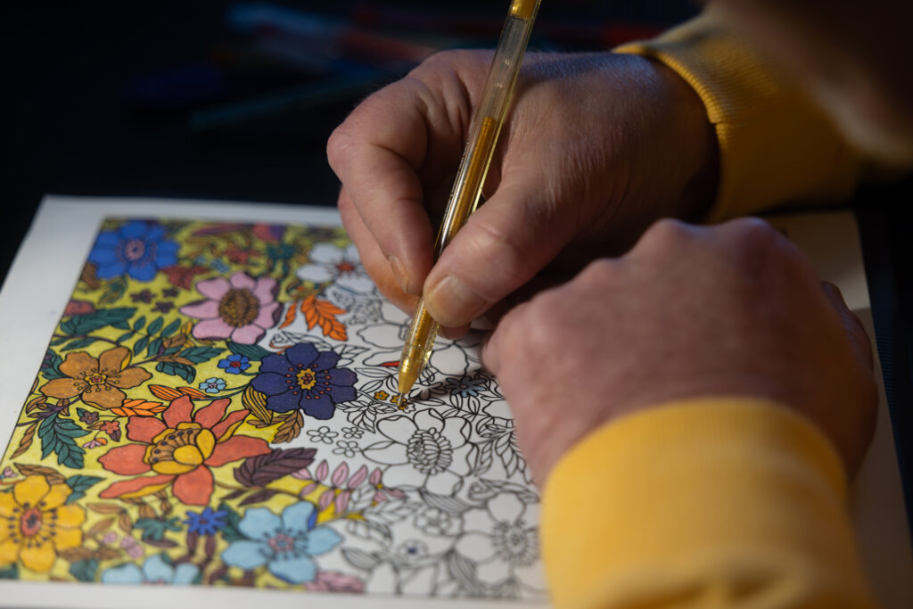 Close up photo of the hands of an older man, using a pen to colour in a drawing.