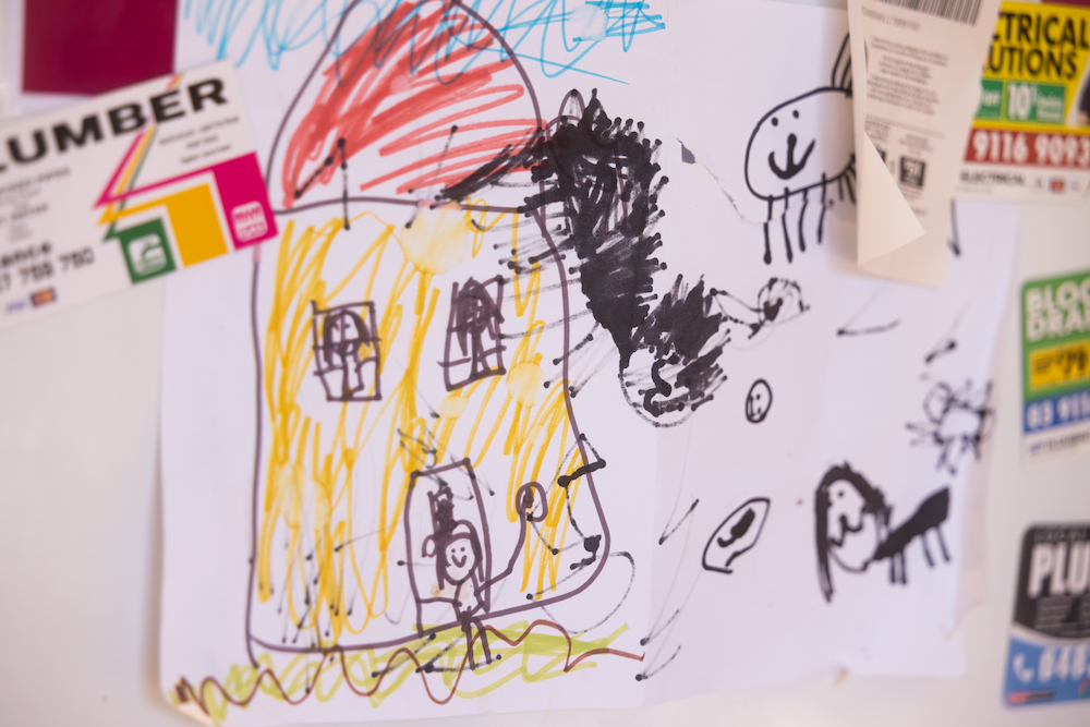 Photo of a child's drawing of a house, displayed on a fridge, supported by magnets.