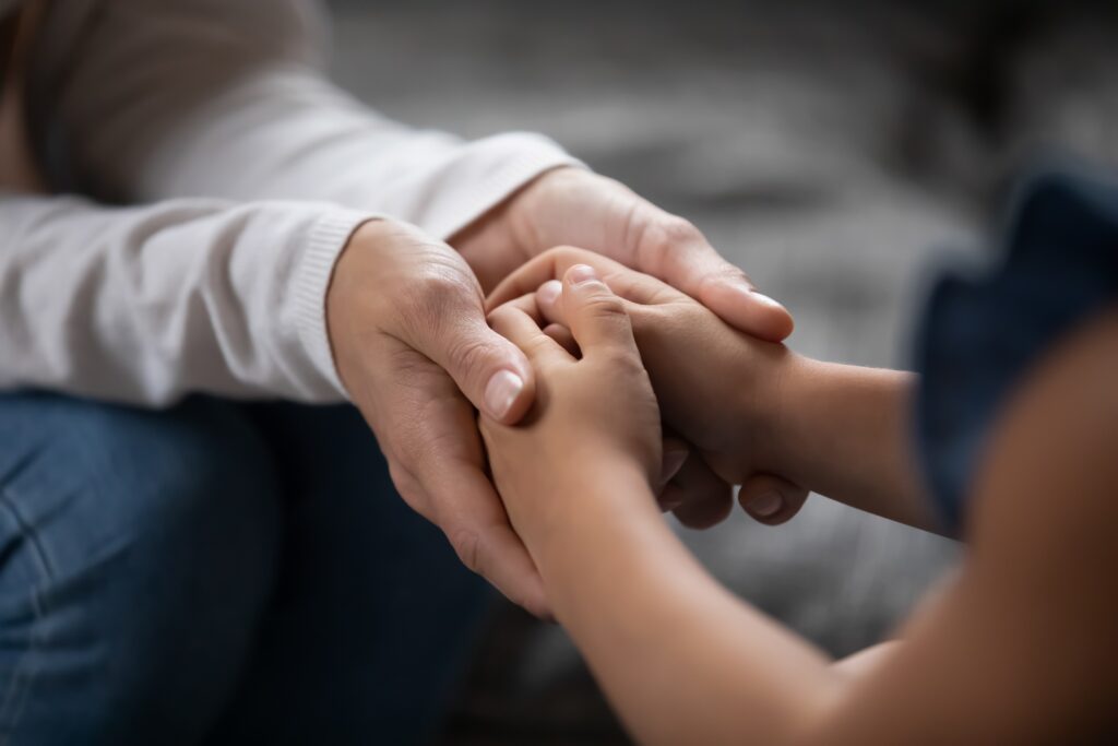 Close up photo of the hands of a child being cradled by the hands of an adult woman.